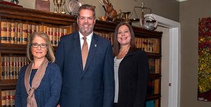 Larissa, Robert and Gina standing in front of the bookcase full of law books.